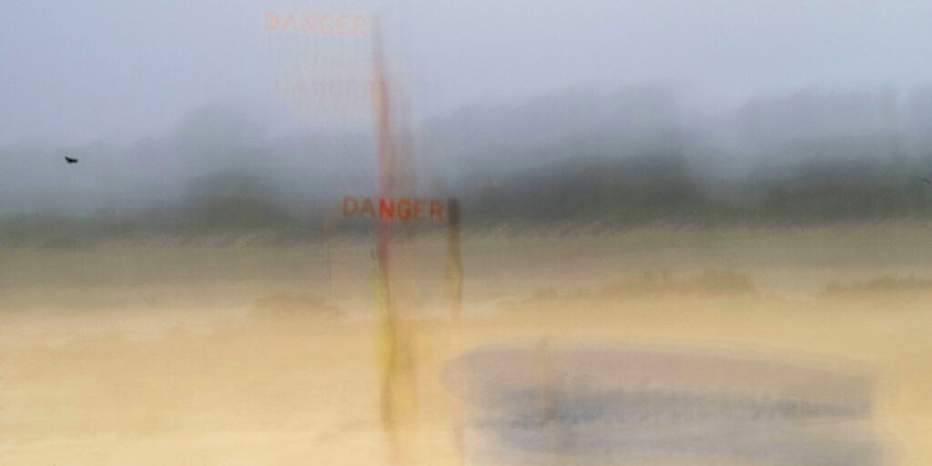 Photographie « Danger », série Songes de Sabine Chabot : Un panneau Danger sur la plage resiste aux bourrasques.